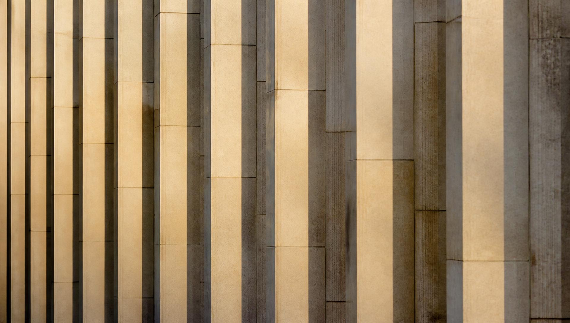Repeating vertical stone fins of a civic building facade in raking afternoon light